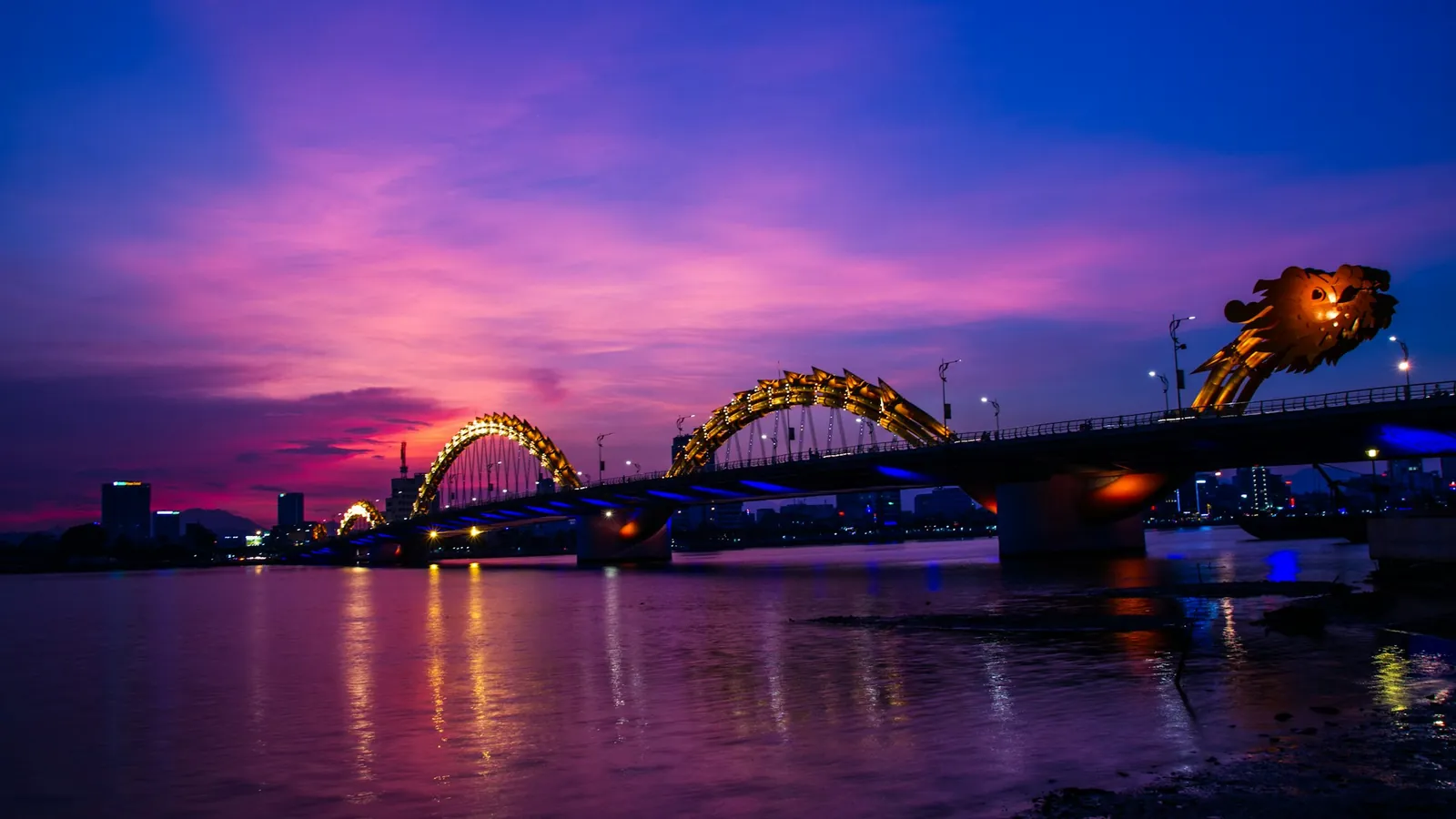 Dragon Bridge i Da Nang lyser opp over Han-elva under en lilla solnedgangshimmel