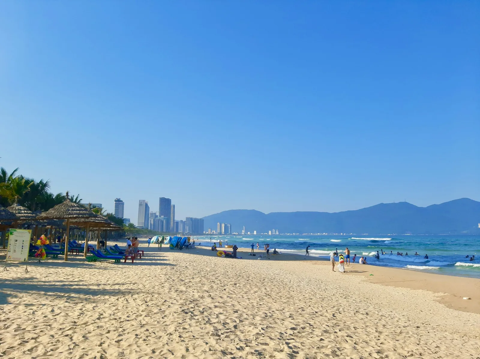 Sandstrand med solstoler og høyhus i bakgrunnen ved My Khe-stranden i Da Nang