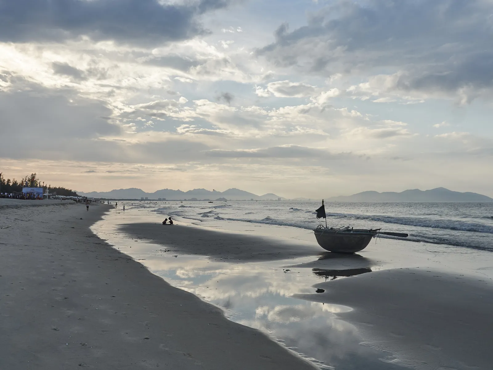 Rund kurvbåt på stranden ved An Bang i Hoi An i kveldslys, med fjell langs kysten bak