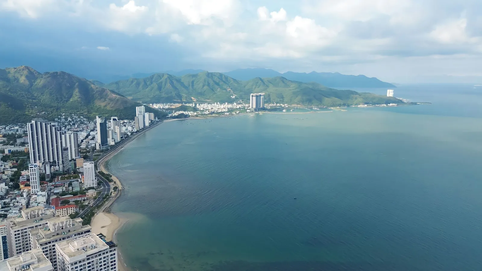 Nha Trang-bukta sett ovenfra, med strandpromenade, høyhus og grønne fjell bak