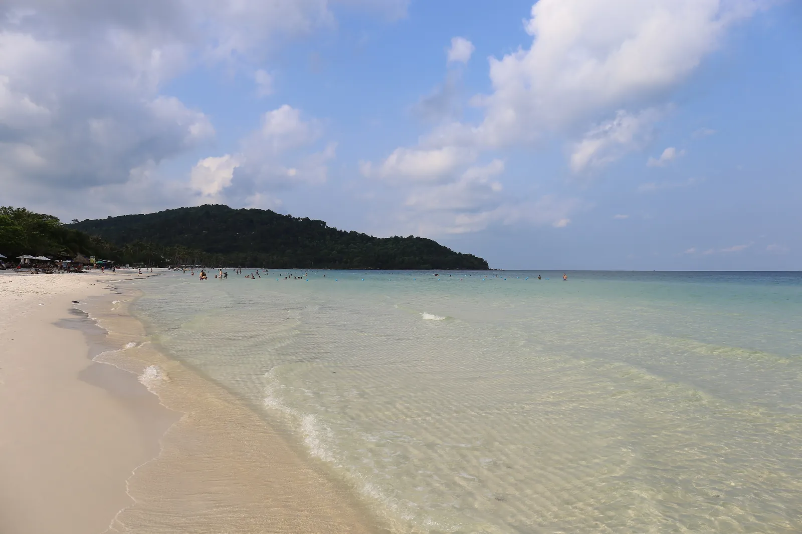 Hvit sand og grunt, klart vann ved Sao Beach på Phu Quoc, med skogkledd odde bak