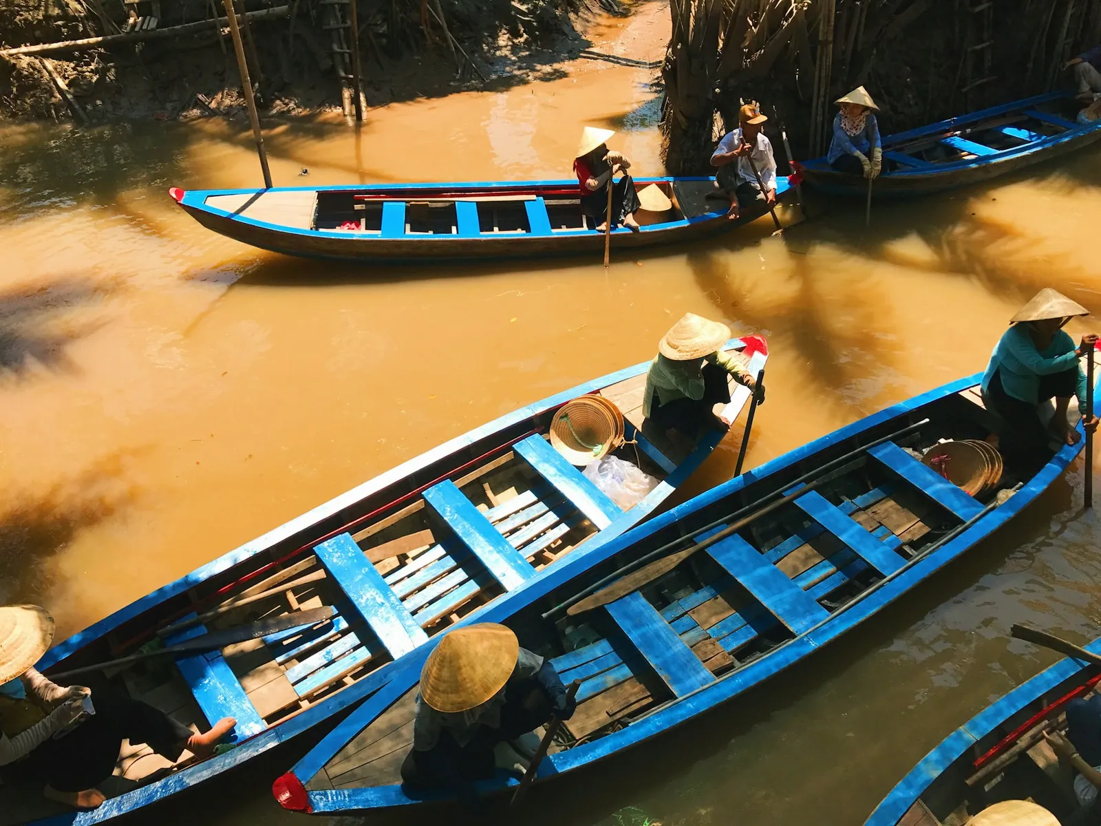 Blå trebåter med roere på brun kanal i Mekongdeltaet