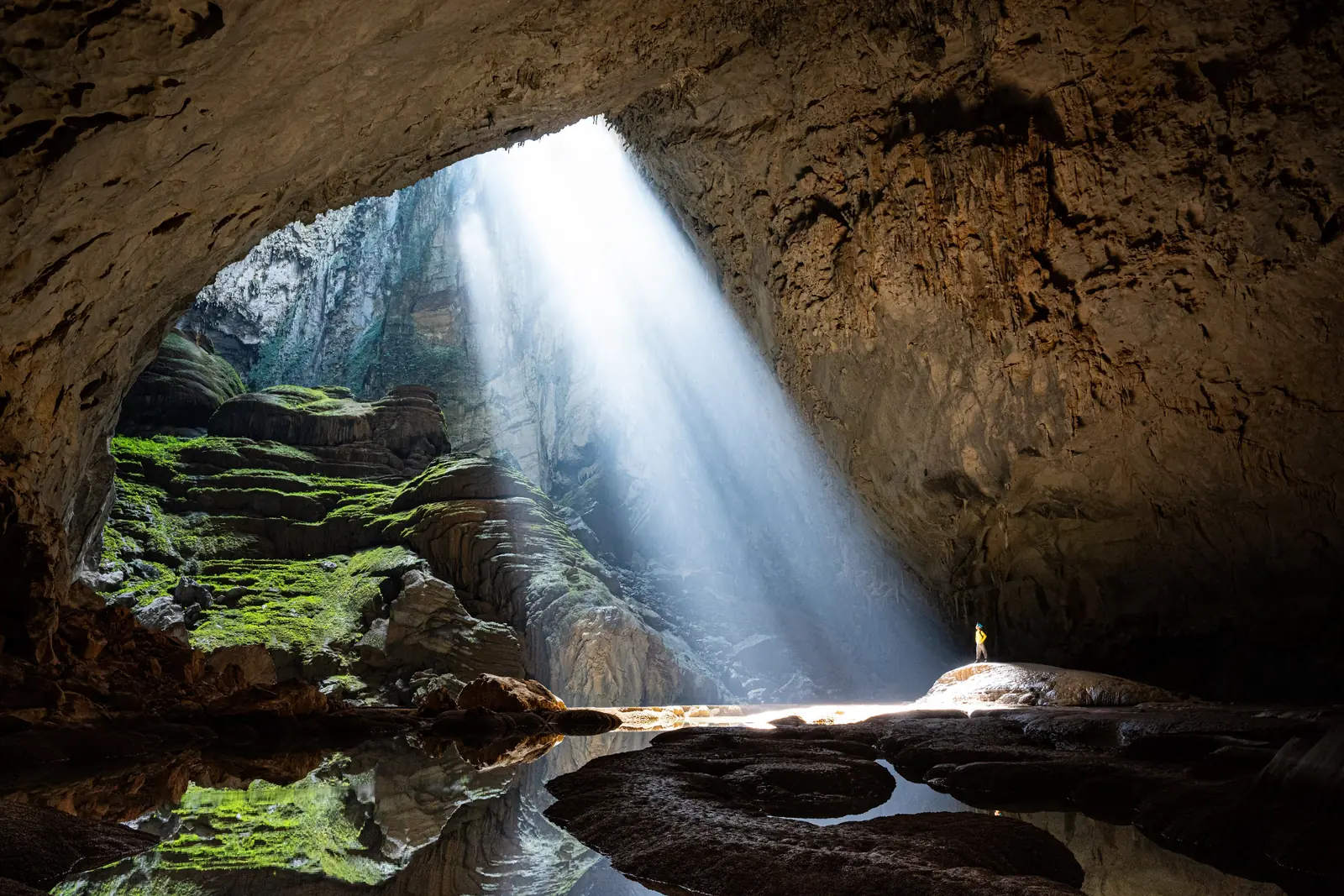Solstråle som trenger ned i den enorme Son Doong-grotta med en liten turgåer ved vannkanten