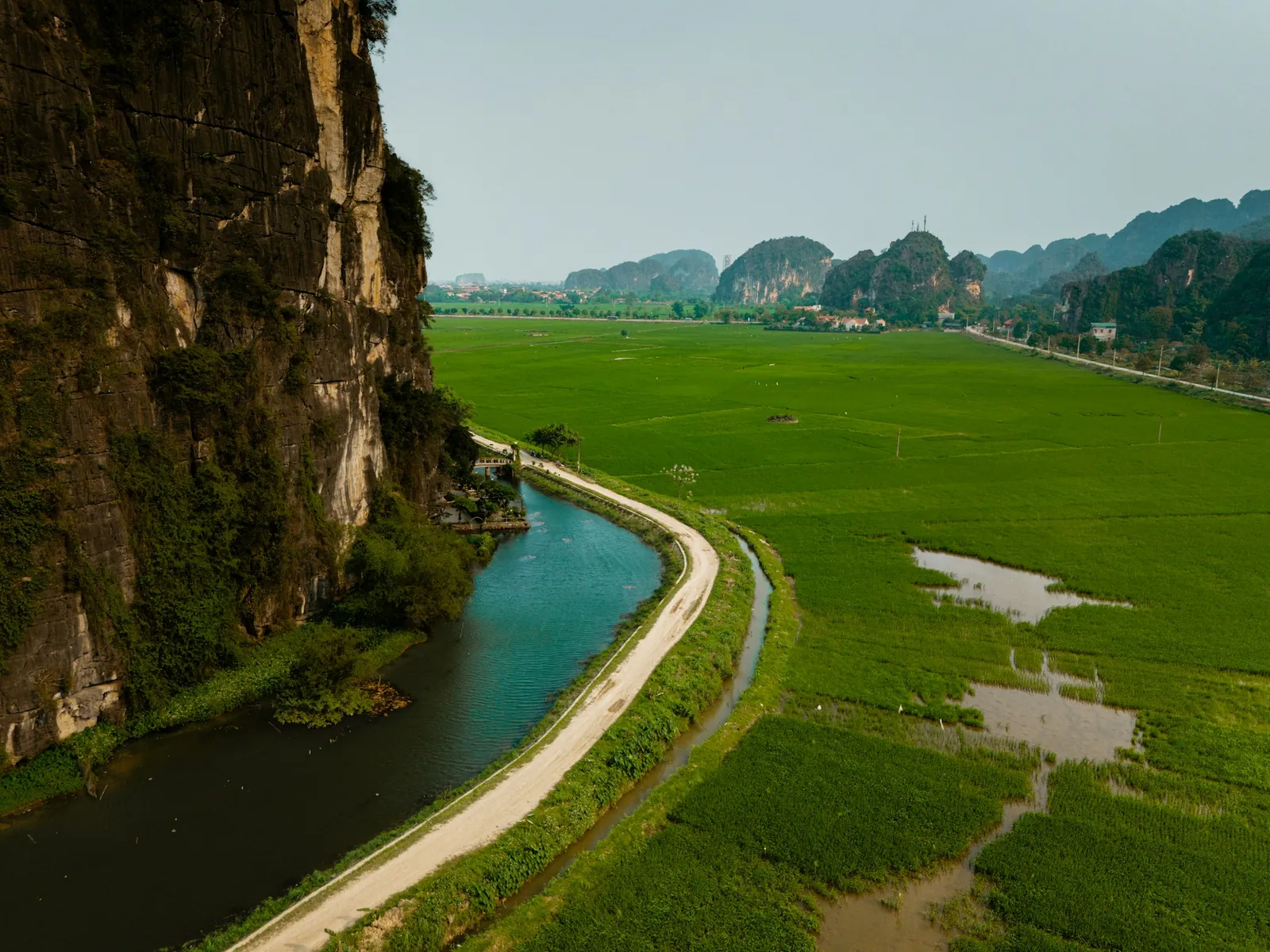 Grusvei langs en kanal mellom kalksteinsklippe og grønne risåker ved Ninh Binh