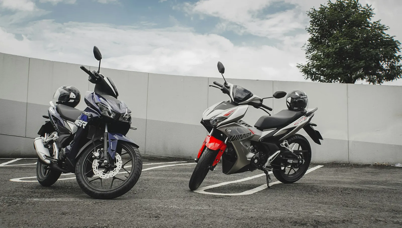 To Honda Winner-motorsykler med hjelmer parkert på en parkeringsplass