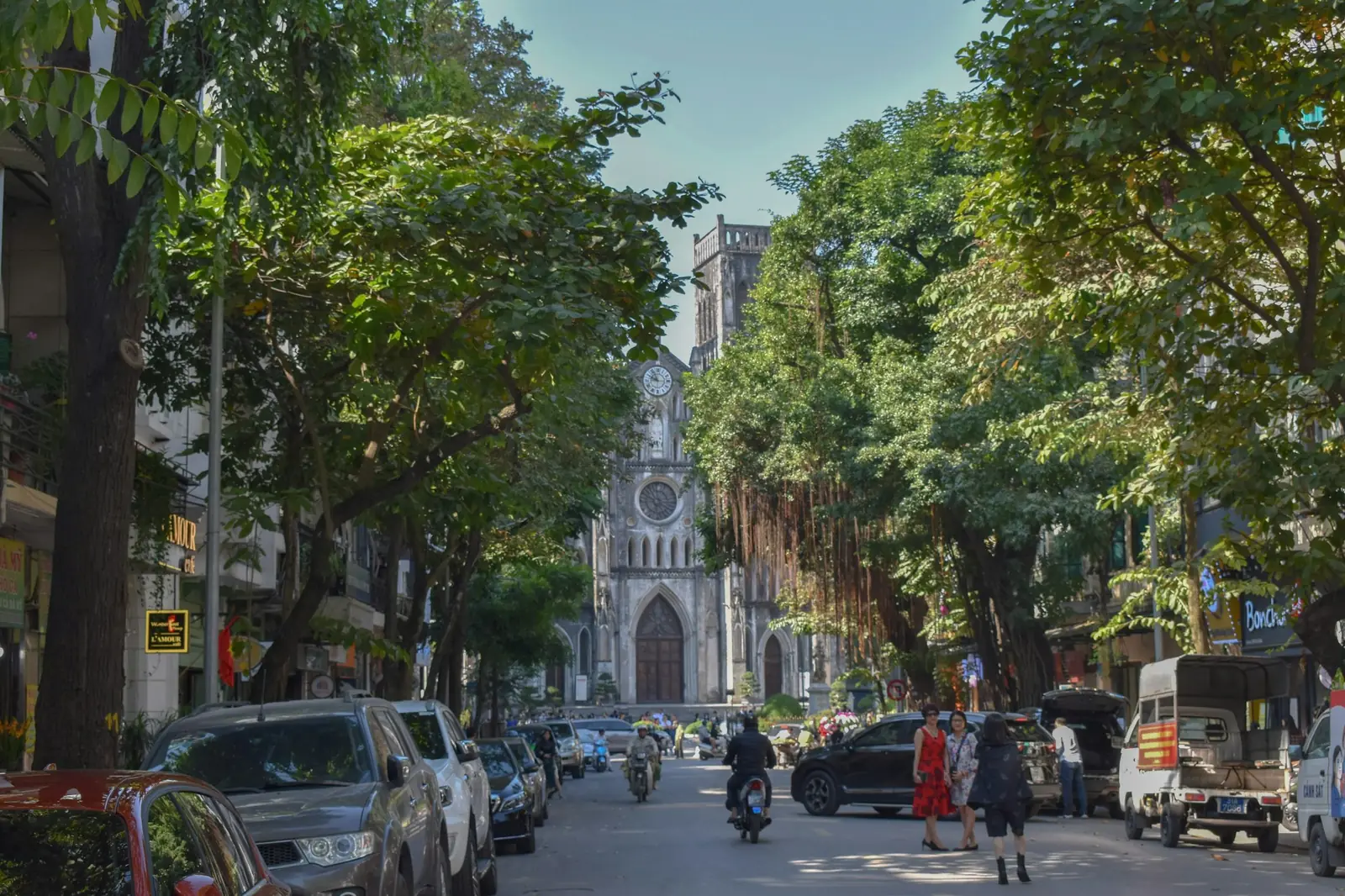 Trelagt gate i Hanoi med Sankt Josefs katedral i enden og mopeder og parkerte biler langs veien