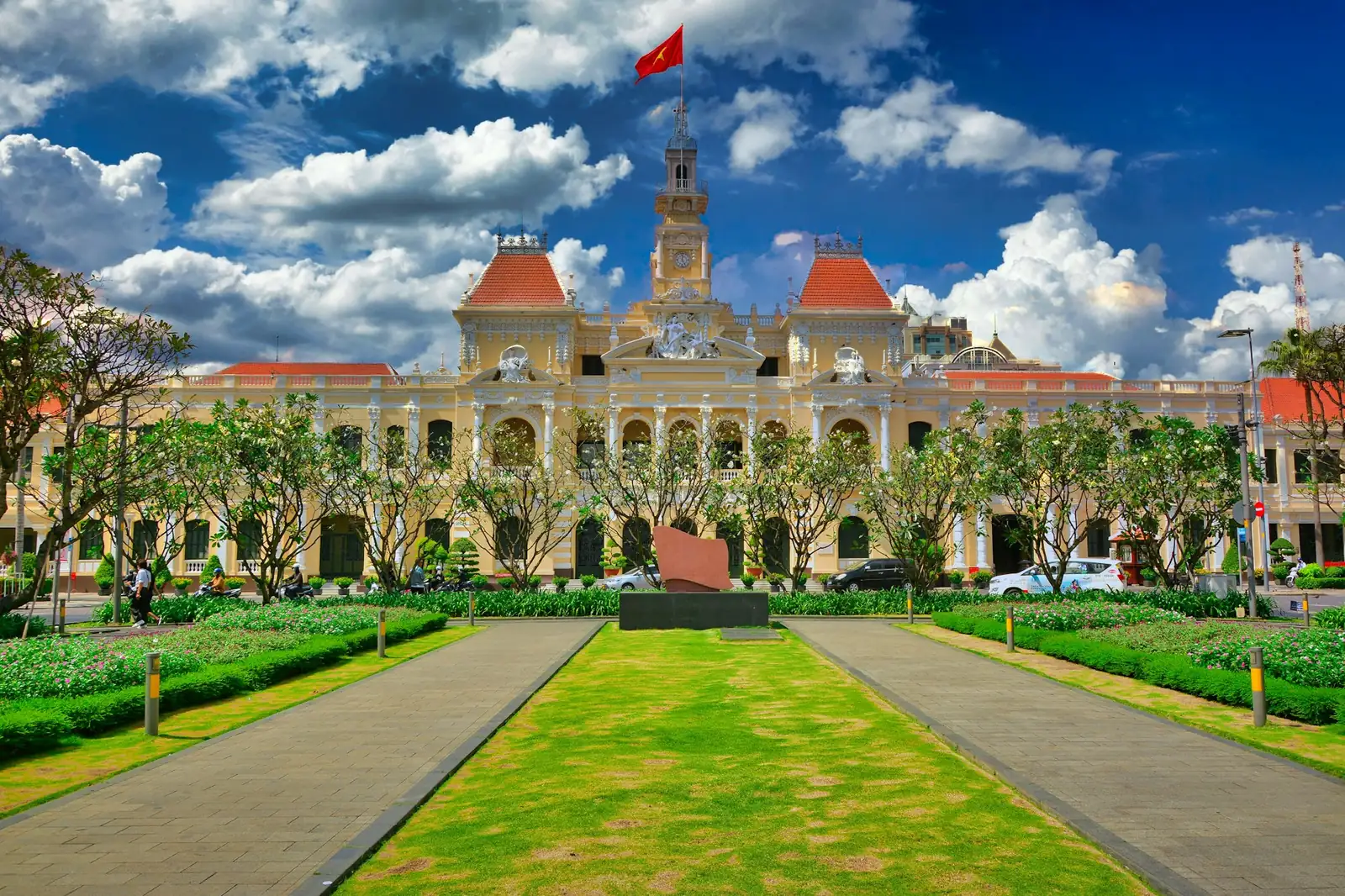 Ho Chi Minh-byens folkekomité i gul fransk kolonialstil med vietnamesisk flagg og grønn plen foran