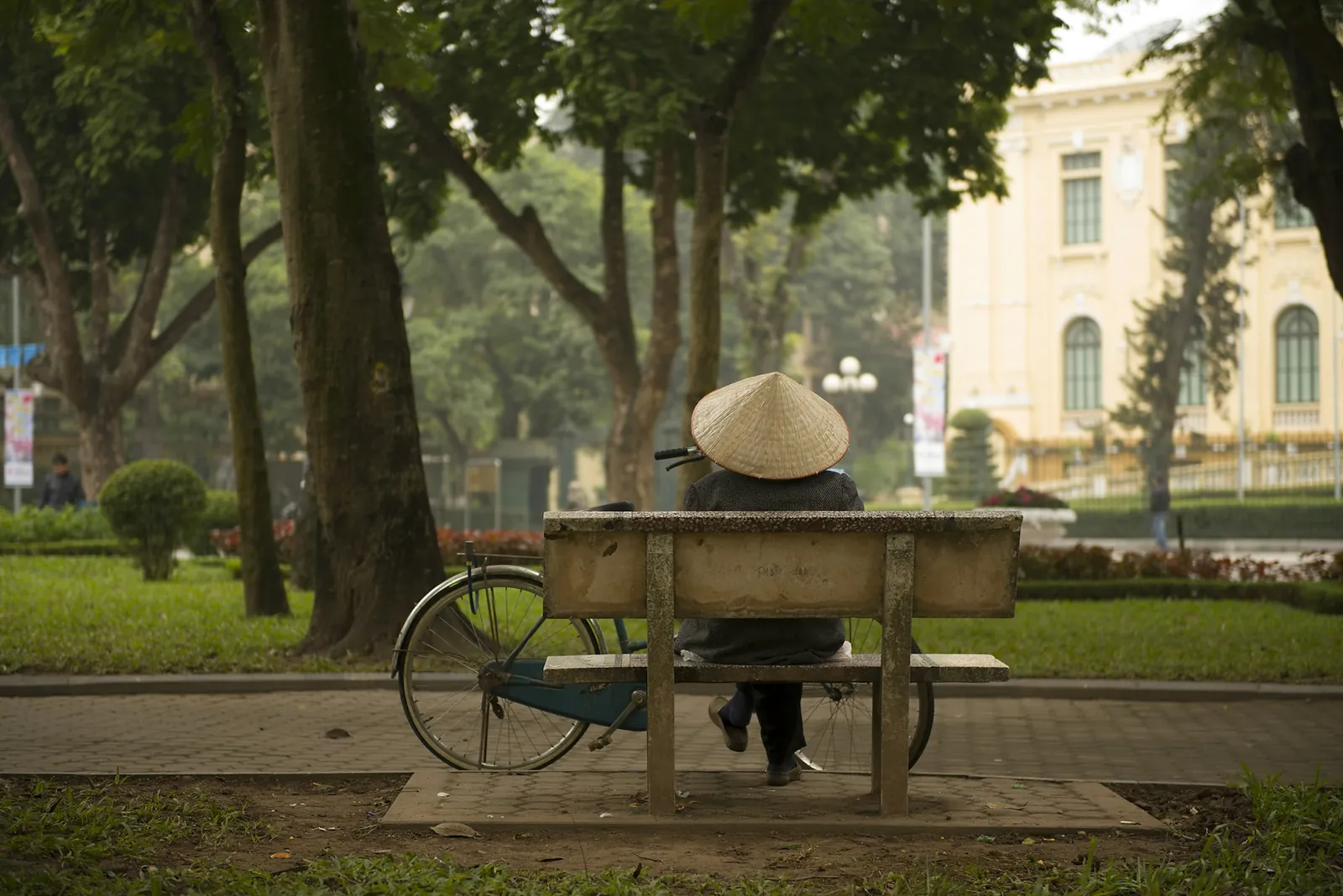 Mann med kjegleformet hatt hviler på en parkbenk i Hanoi