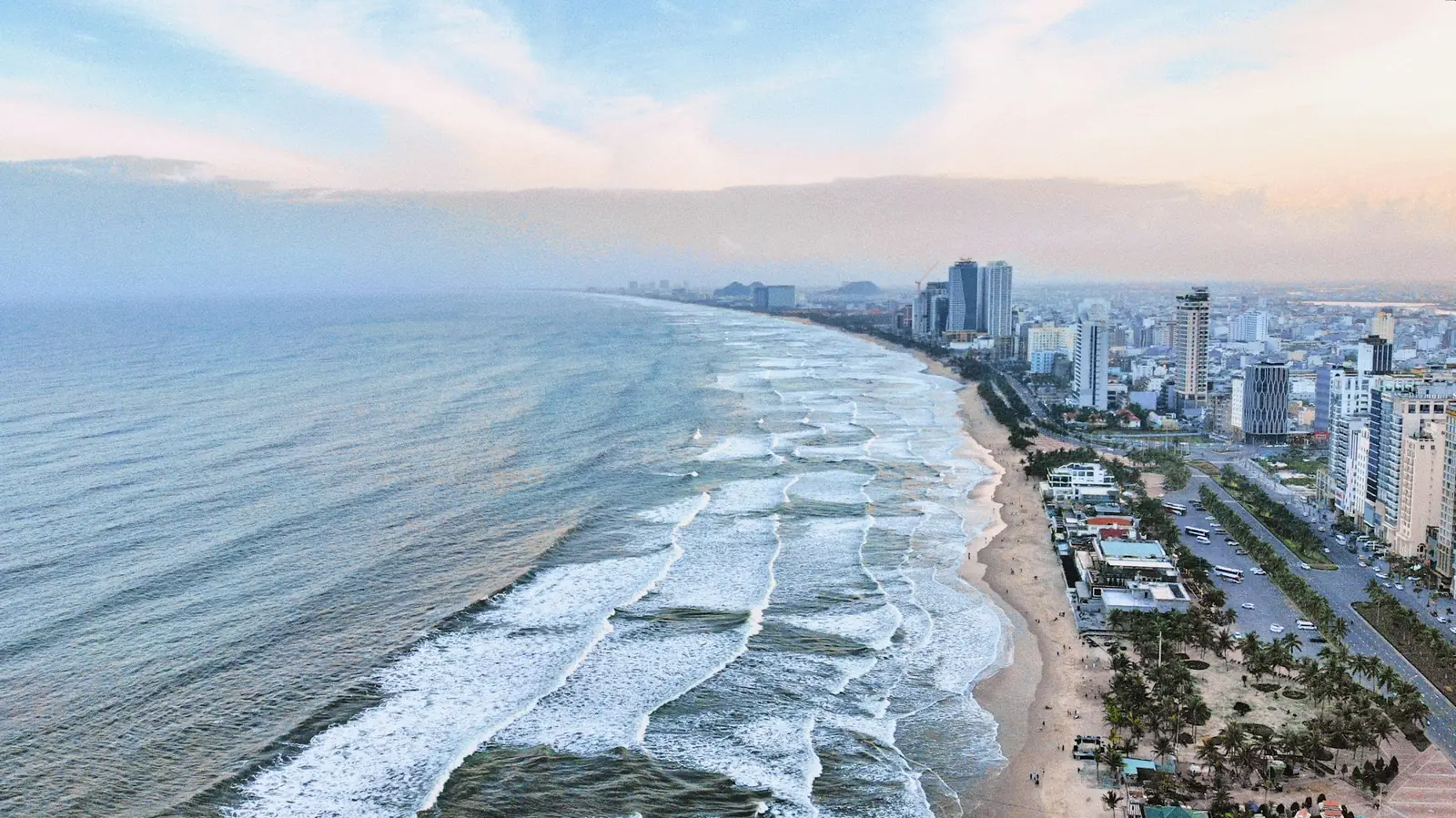 Flyfoto av bølger som ruller inn mot stranden i Da Nang med hoteller og høyhus langs kysten