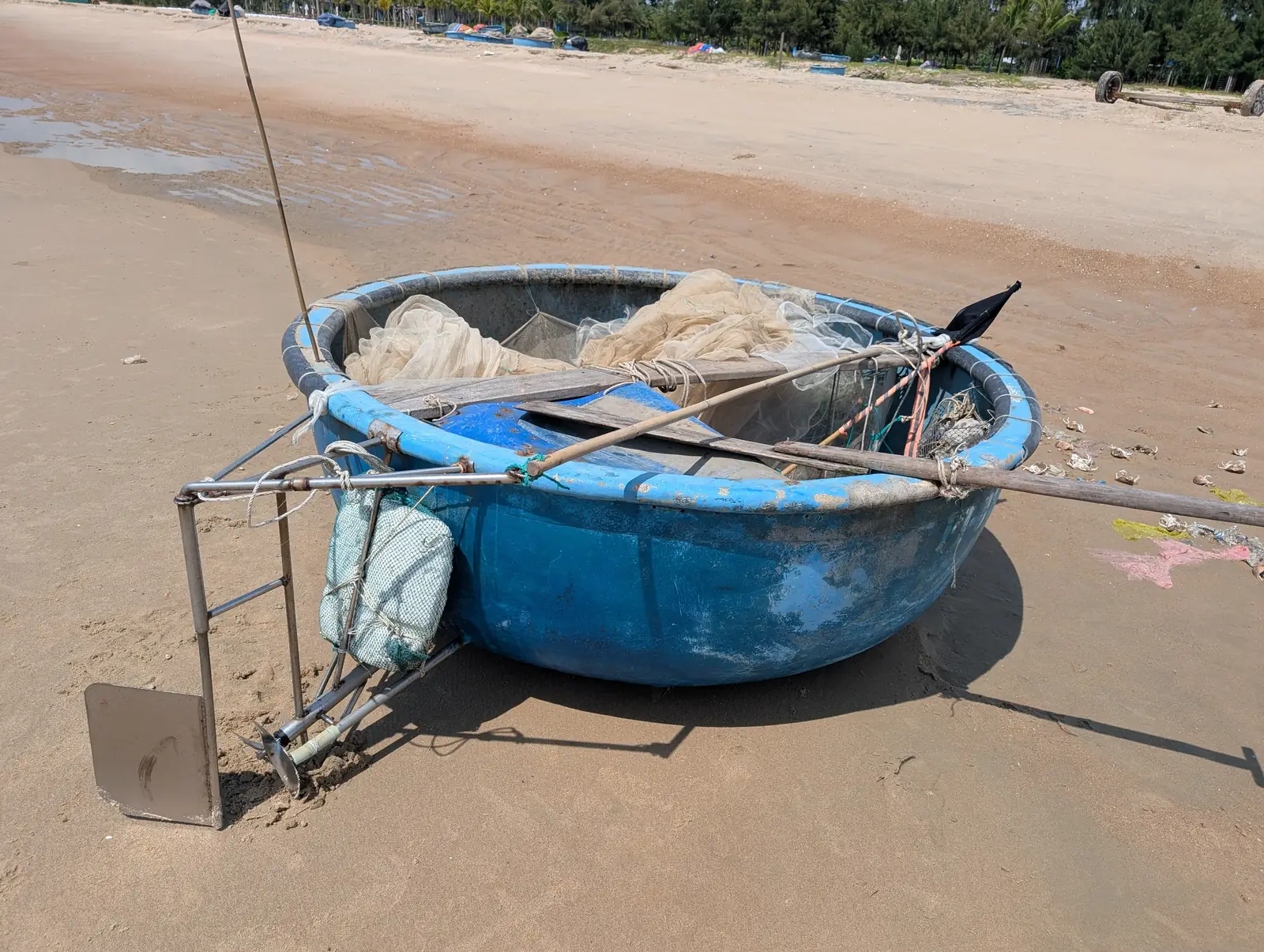 Blå kurvbåt med fiskenett på sandstranden ved Ho Tram