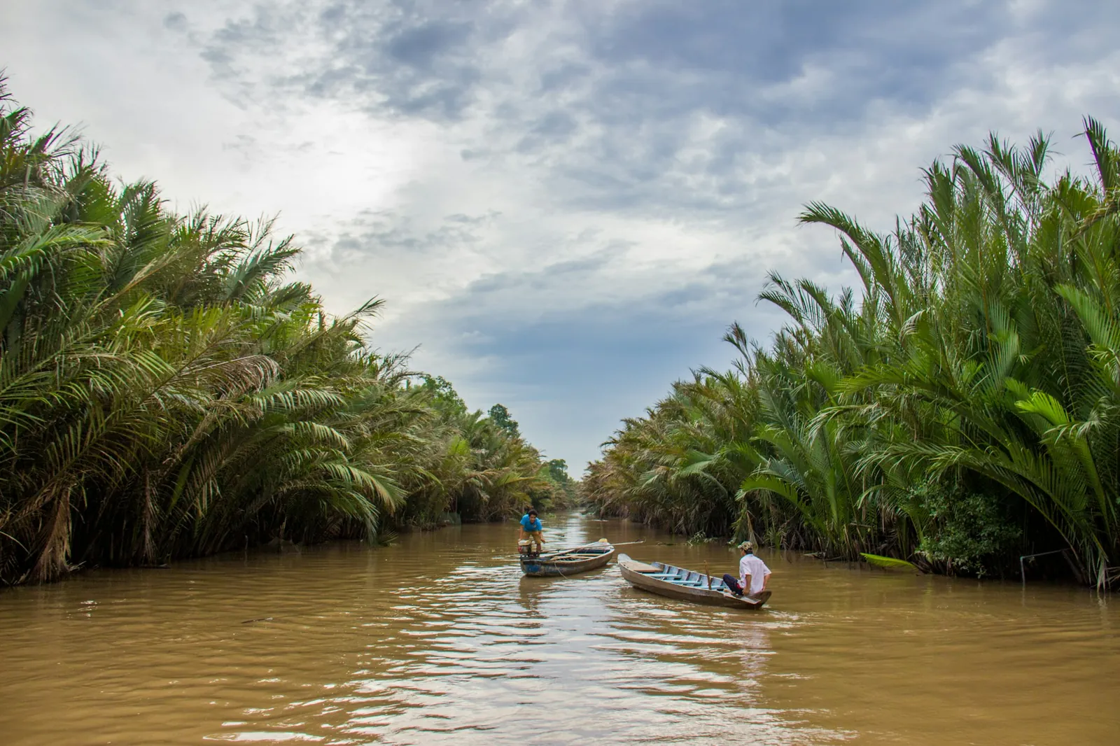 Smal kanal i Mekongdeltaet omkranset av nipapalmer, med småbåter på brunt vann