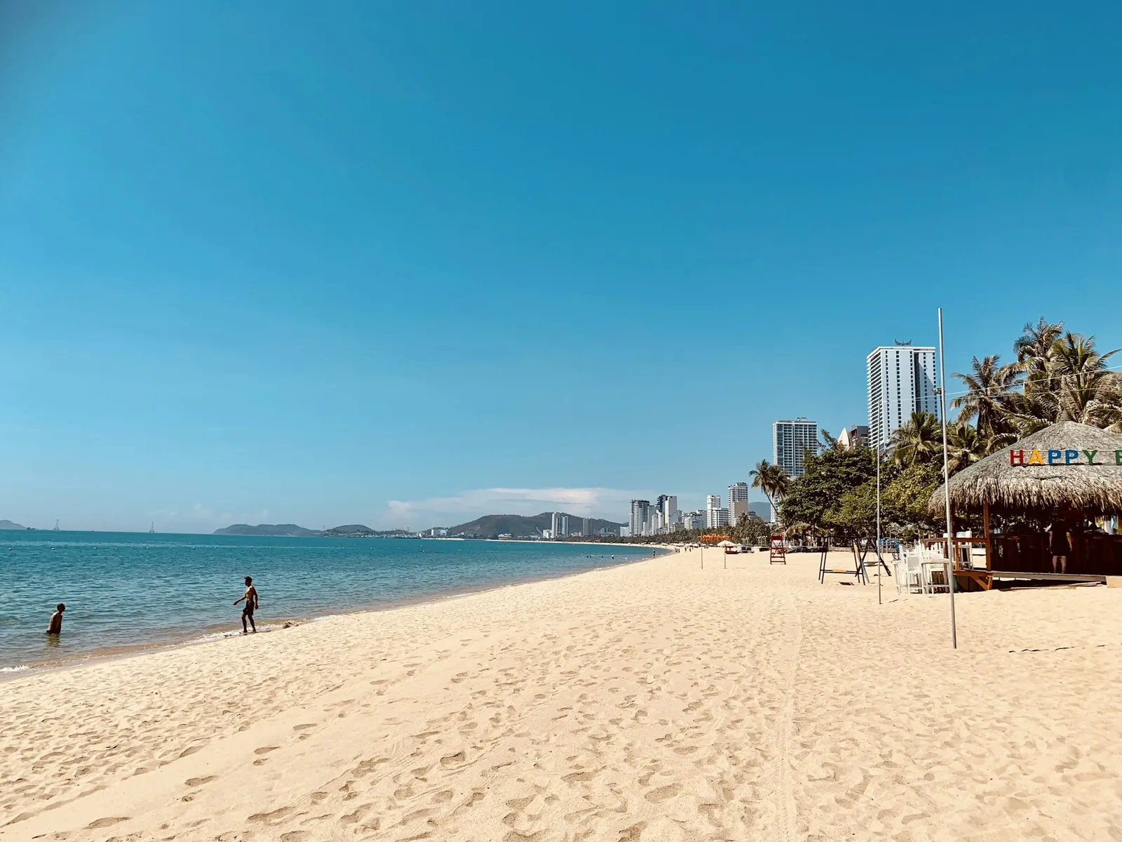 Sandstrand i Nha Trang med palmer, strandhytte og høyhus langs kysten