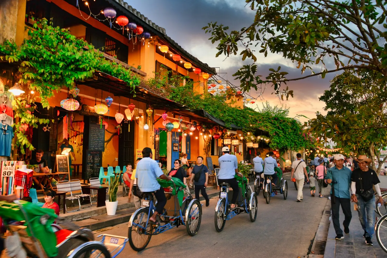 Livlig gate i gamlebyen i Hoi An i skumringen med lykter, kafeer og sykkeltaxier