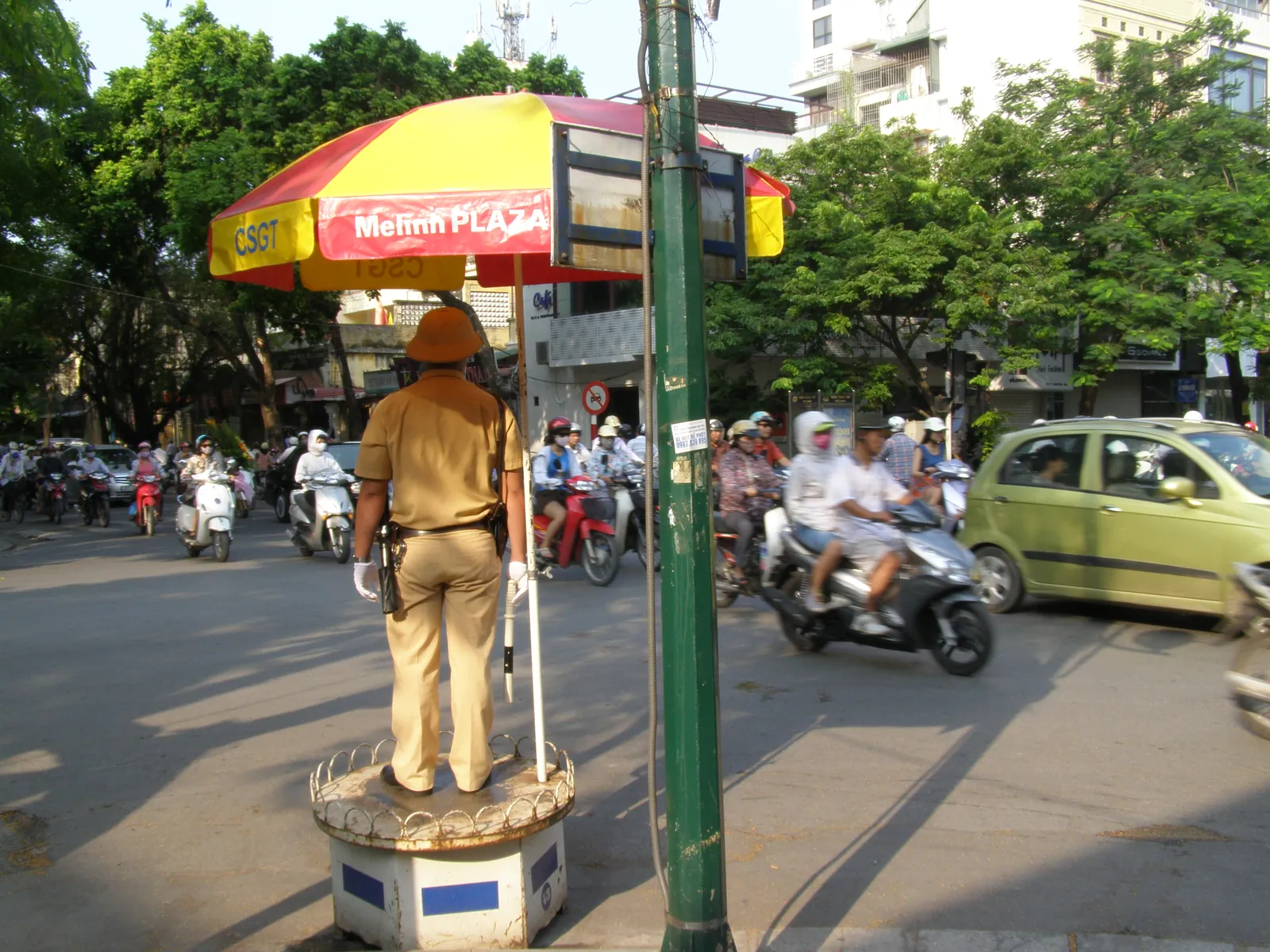 Trafikkpolitibetjent på podium med parasoll ved et veikryss i Hanoi, med motorsykler