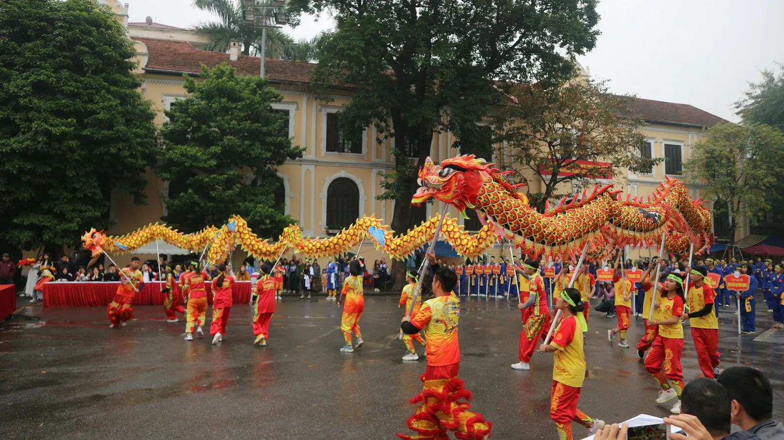 Dragedans i gul og rød drakt foran en gul kolonialbygning i Hanoi