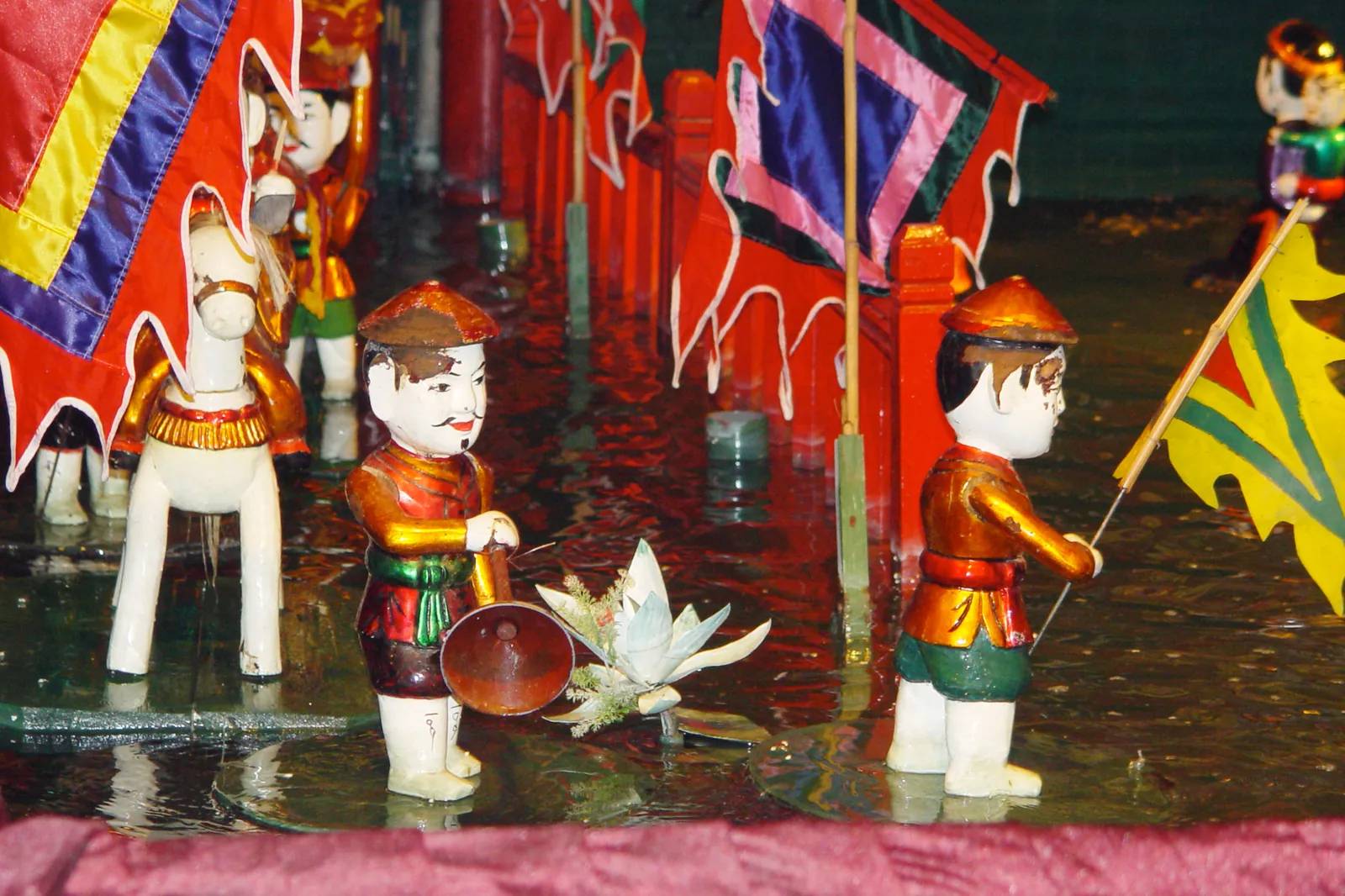 Vannmarionetter med flagg og lotusblomst i vannet under en forestilling i Hanoi