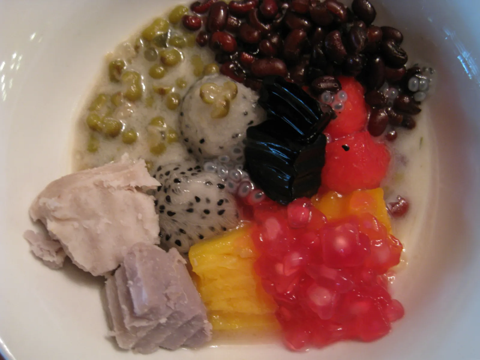 Chè thập cẩm i en hvit skål med mungbønner, røde bønner, dragefrukt, taro, mango og gelé