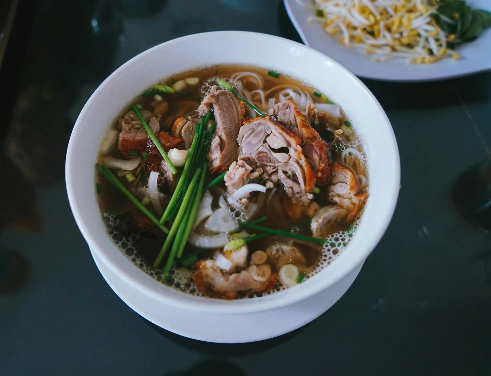 Nudelsuppe med klar buljong, stekt and og vårløk, med bønnespirer ved siden av