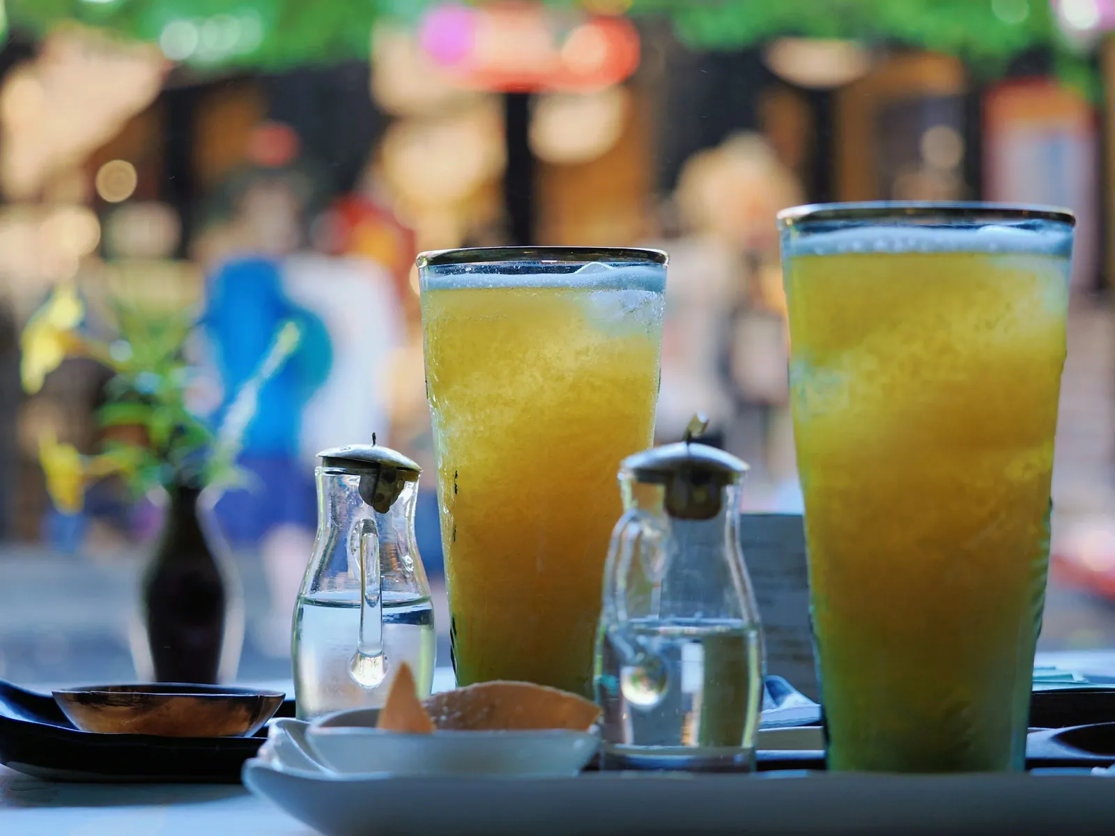 To høye glass med kald gul fruktjuice og is på et kafébord, med små vannkaraffer