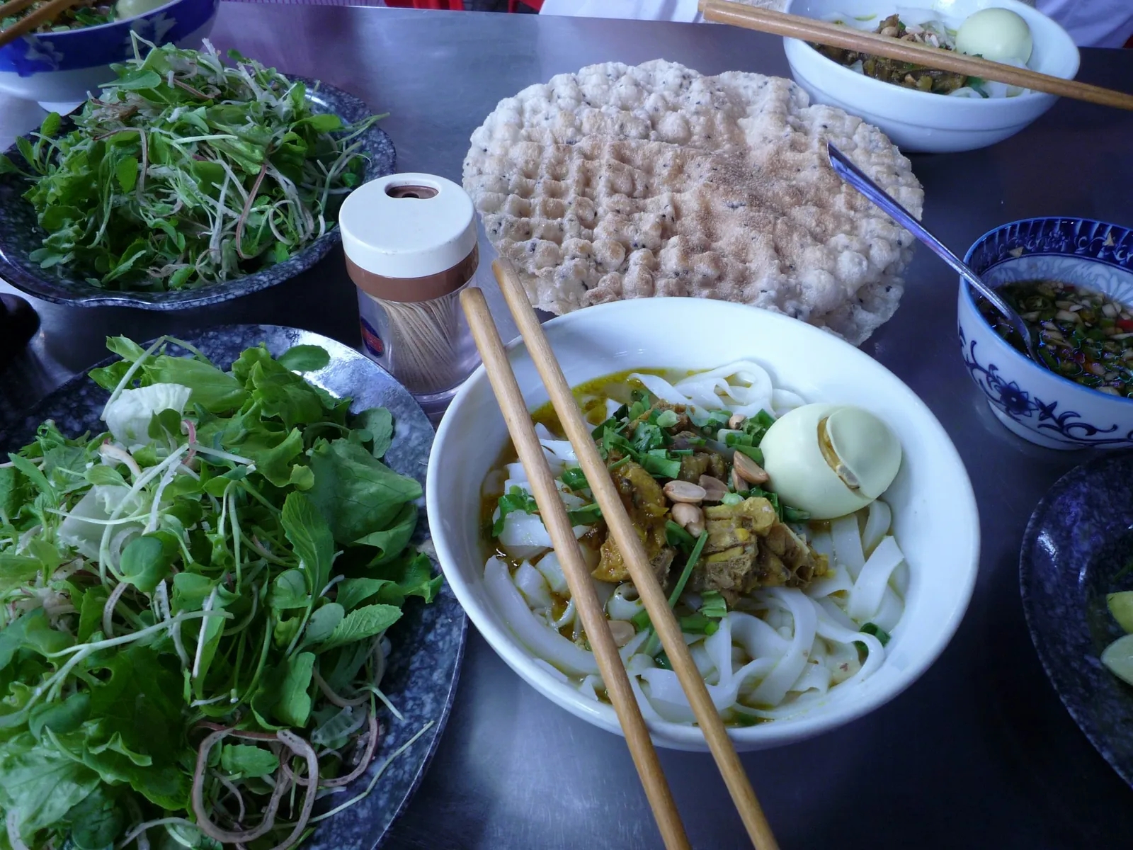 Mi Quang med brede nudler, egg og peanøtter, risknekkebrød og en tallerken med friske urter