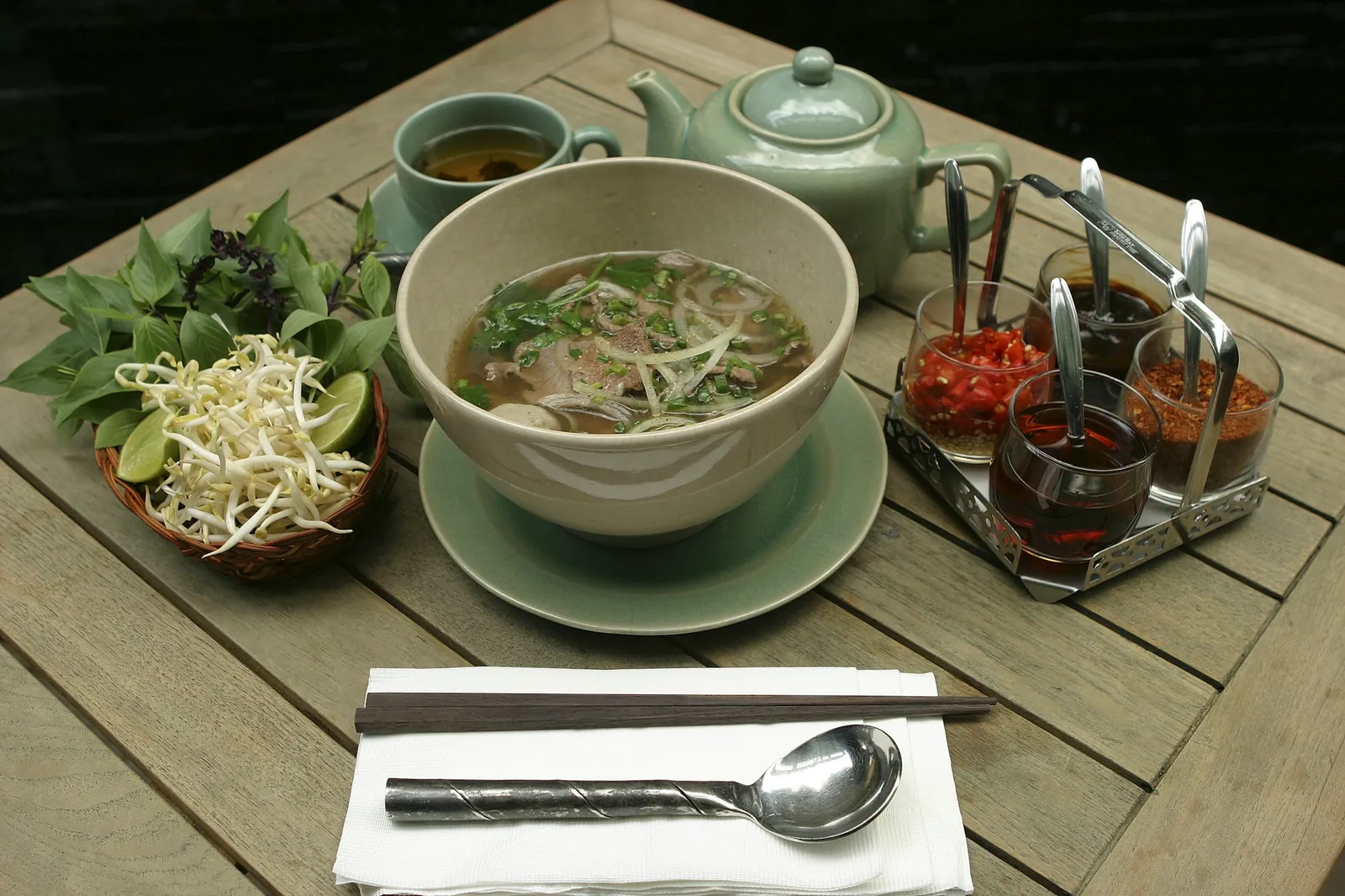 Pho med friske urter, lime, chili og dipsauser på et trebord