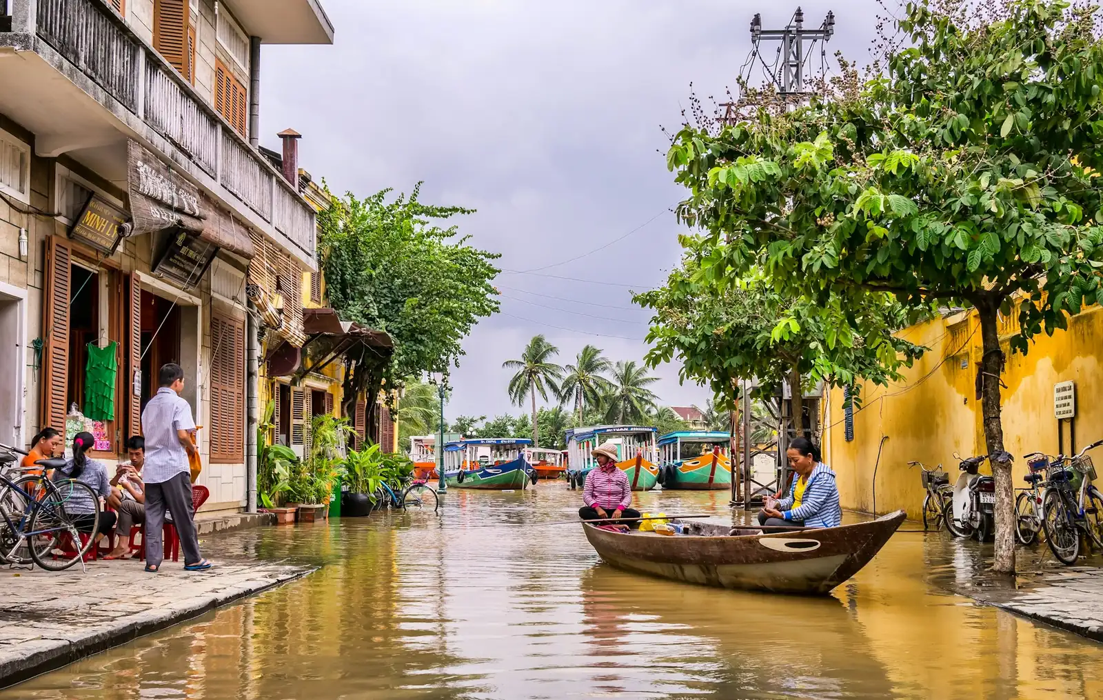 Oversvømt gate i Hoi An der en mann ror en liten båt forbi gule hus