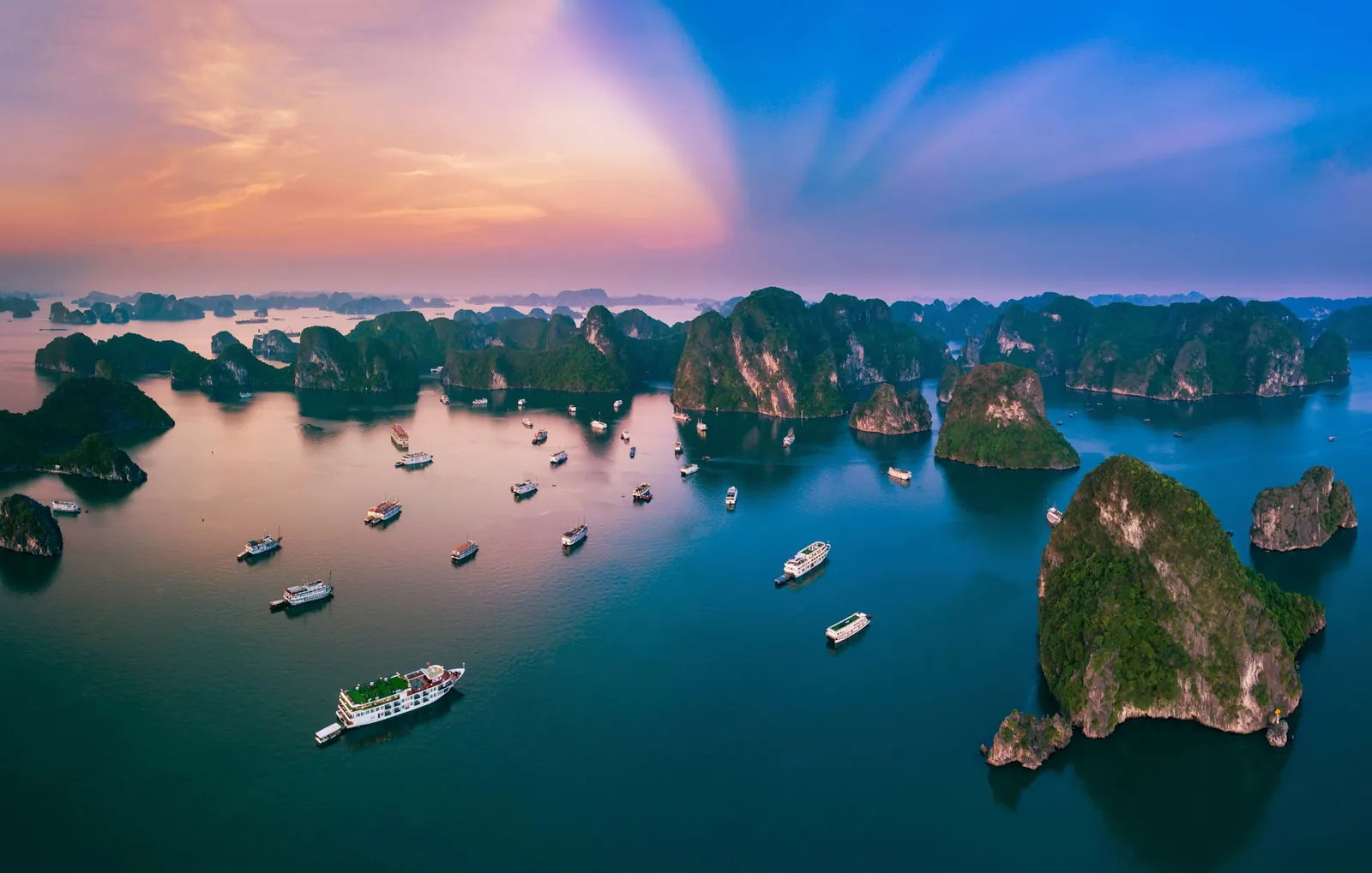Flyfoto av kalksteinsøyer og båter i Ha Long-bukta ved solnedgang