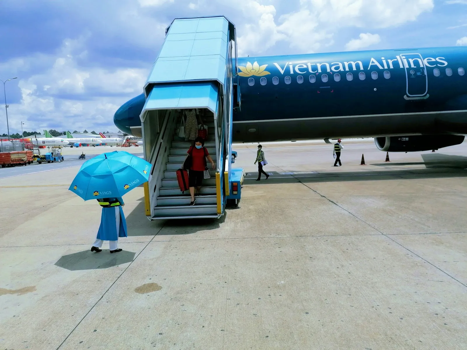 Passasjer med blå paraply går mot flytrappen til et Vietnam Airlines-fly