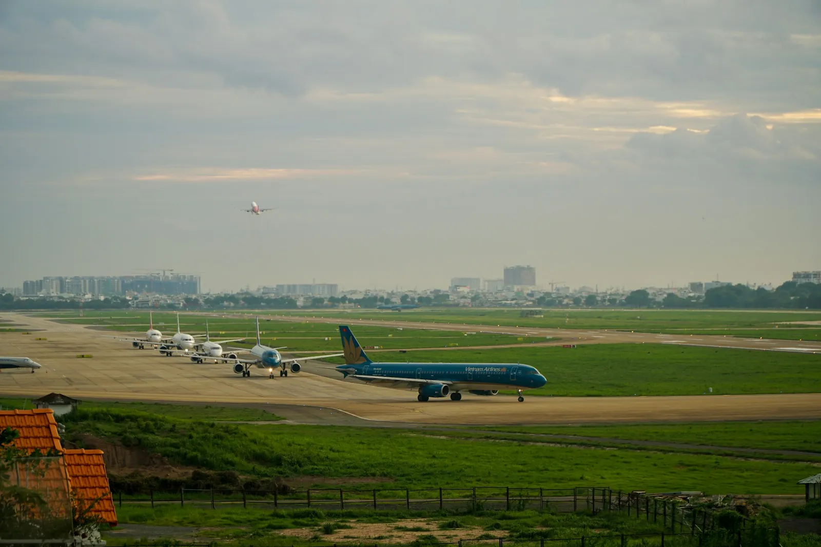 Fly i kø på taksebanen og et fly i luften over en grønn flyplass i Vietnam