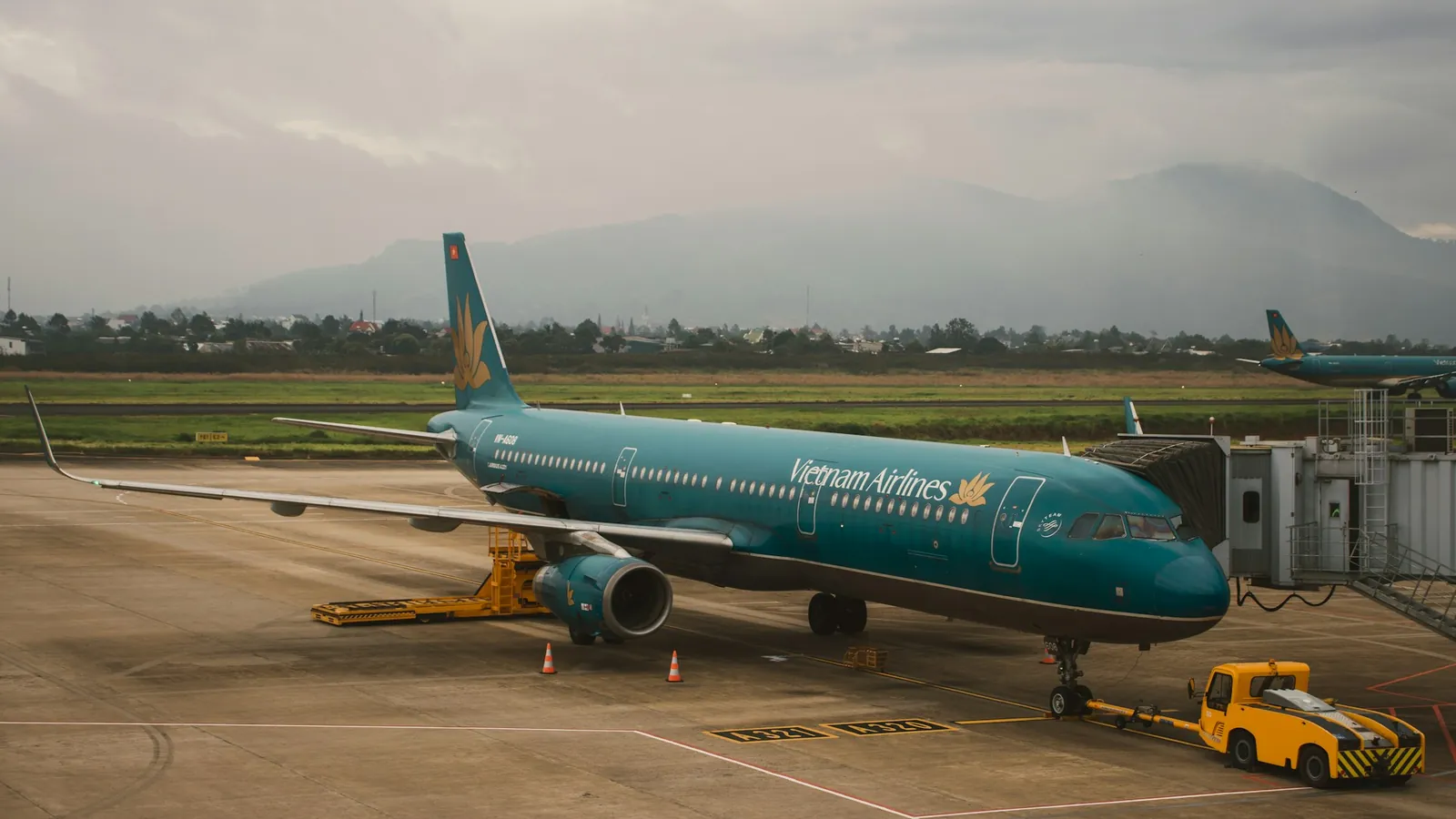 Vietnam Airlines-fly ved gate på en flyplass med fjell i bakgrunnen