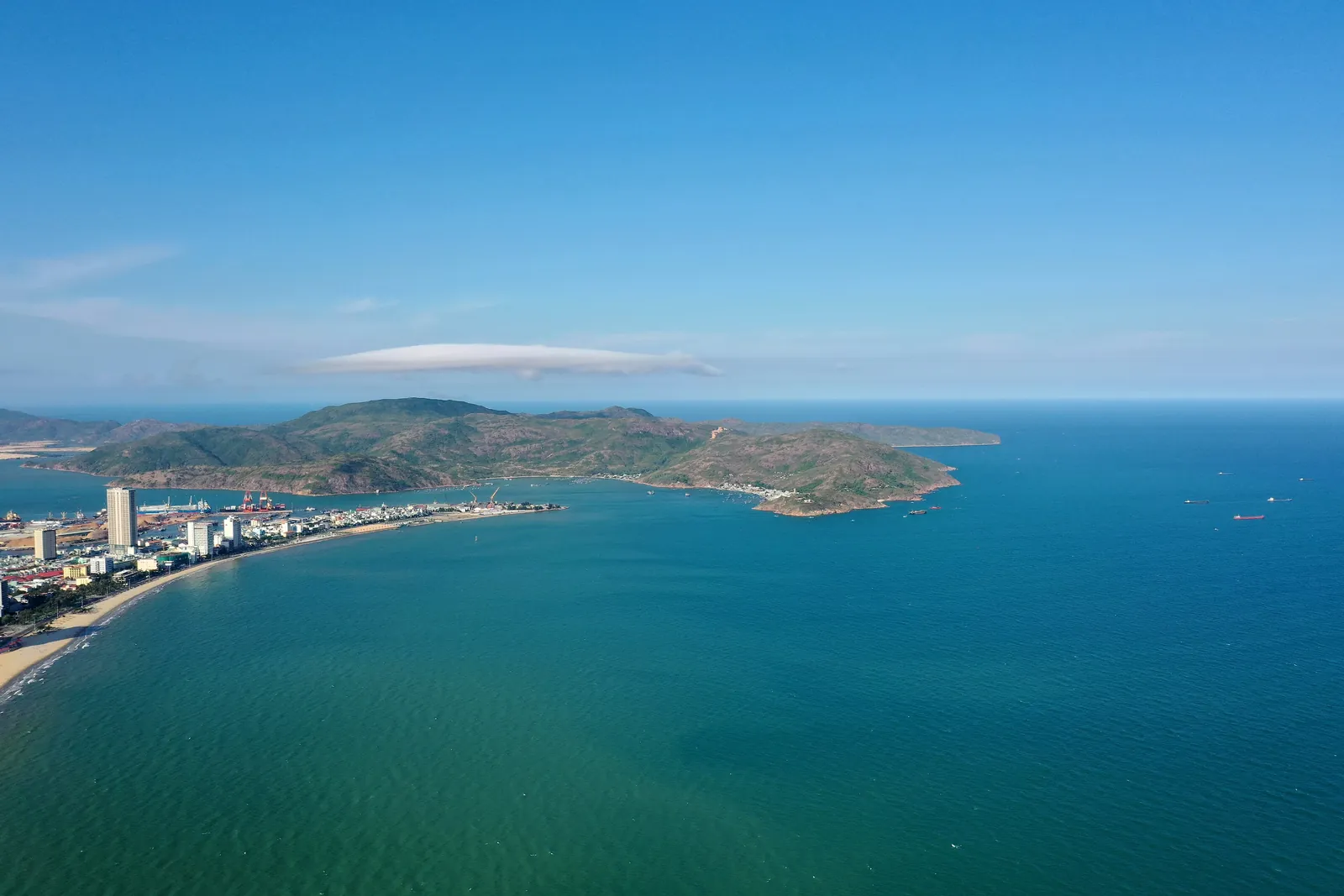 Flyfoto av Quy Nhon-bukta med strandpromenade, byen og en grønn halvøy i horisonten