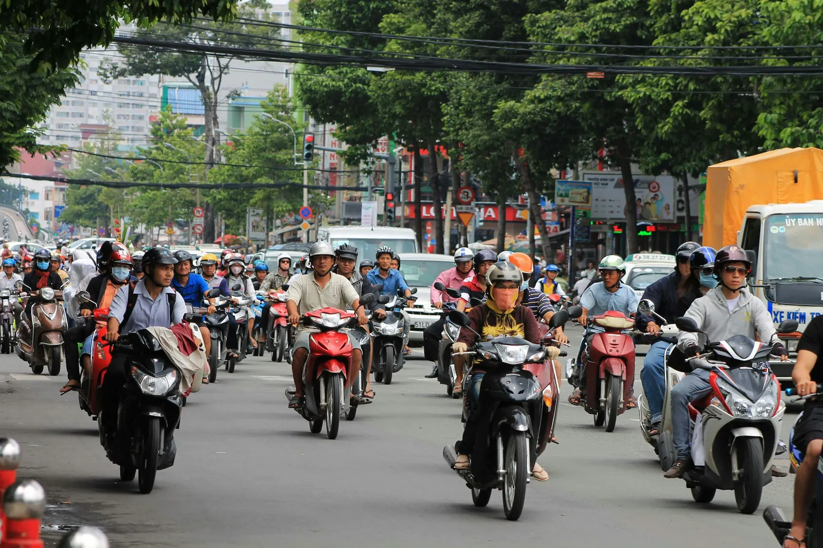 Tett scootertrafikk i en bred, trelagt gate i en vietnamesisk by