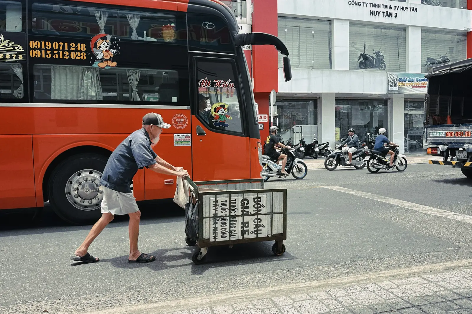 Stor oransje buss i gata mens en mann triller en vogn forbi