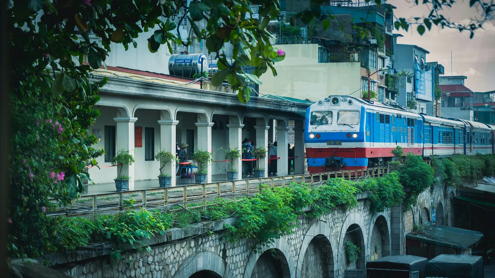 Blått tog på en gammel steinbro gjennom bebyggelsen i Hanoi