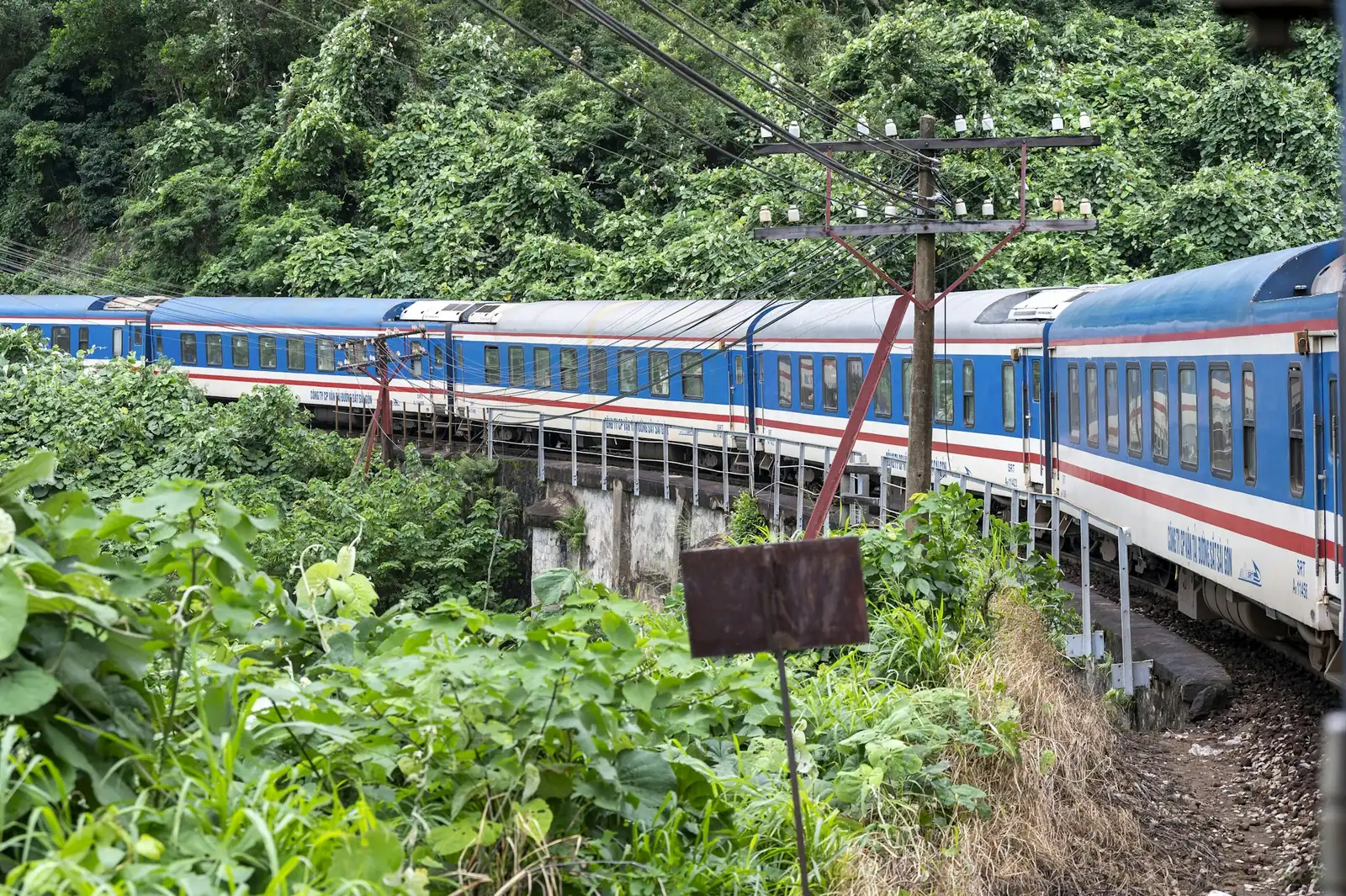 Blått og hvitt tog på Gjenforeningsbanen gjennom frodig skog nord for Da Nang