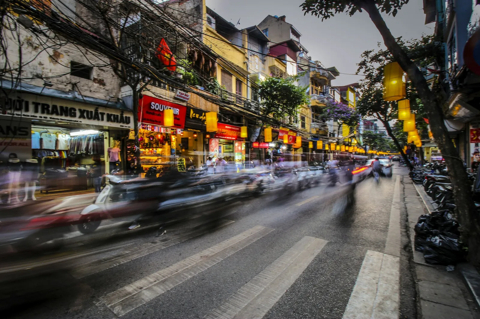 Gate i gamlebyen i Hanoi i skumringen med gule lykter og scootere i bevegelse