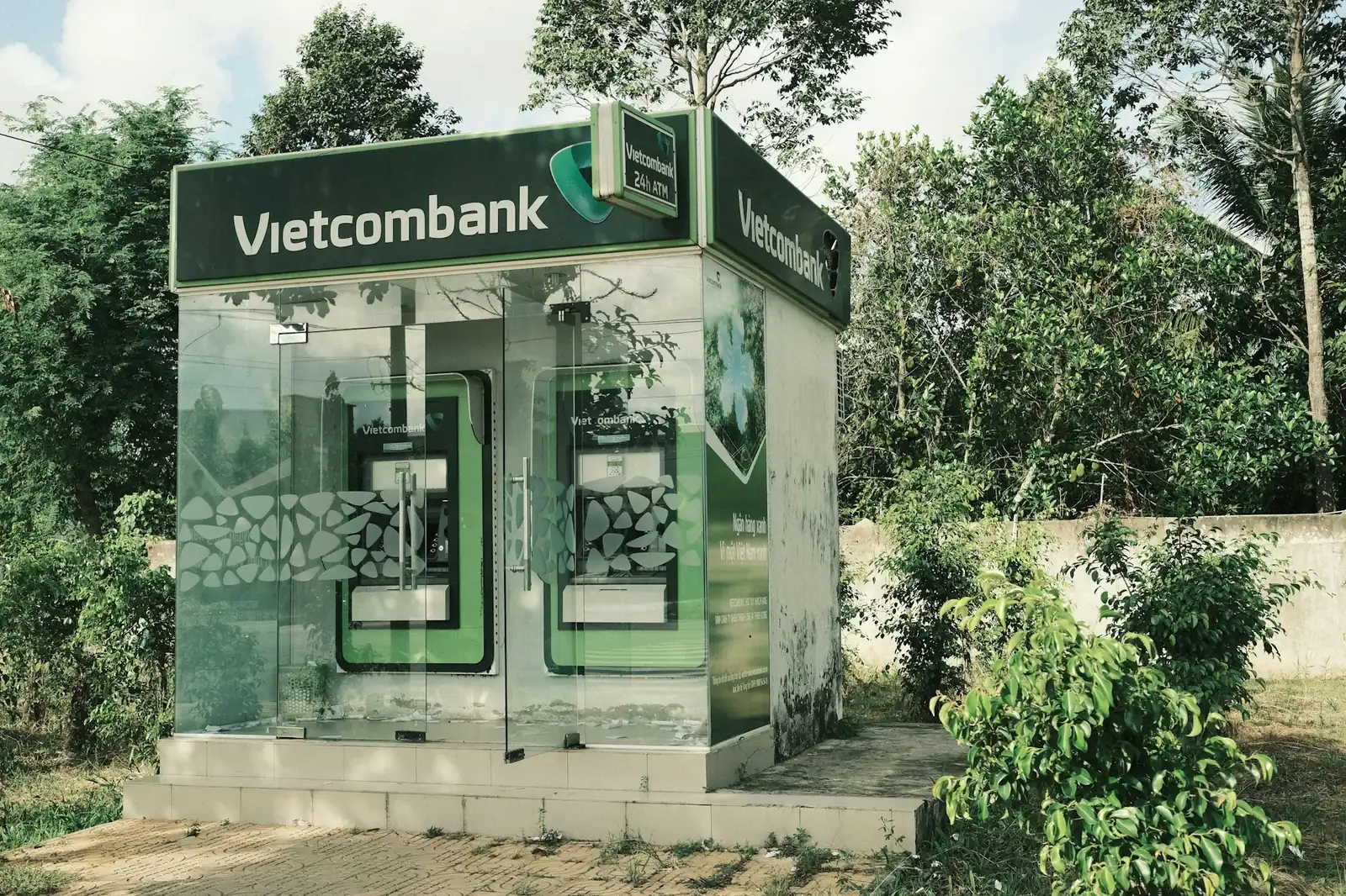 Vietcombank-minibank i et glassbur omgitt av grønne trær og busker i Vietnam